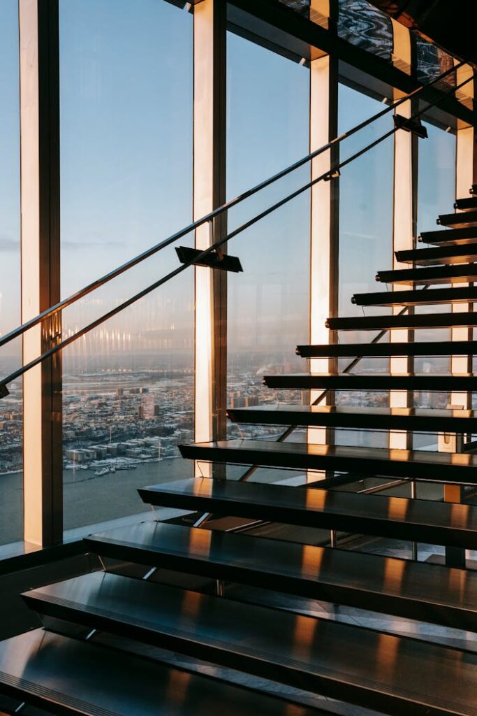 Stairway with metal railing located in contemporary business center with bright sunlight near glass wall overlooking modern city with buildings